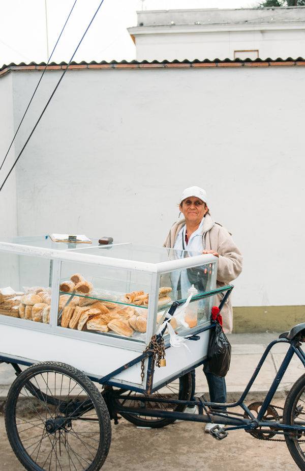 A woman standing behind a rickshaw with a perspex case mounted on it, containing baked goods.