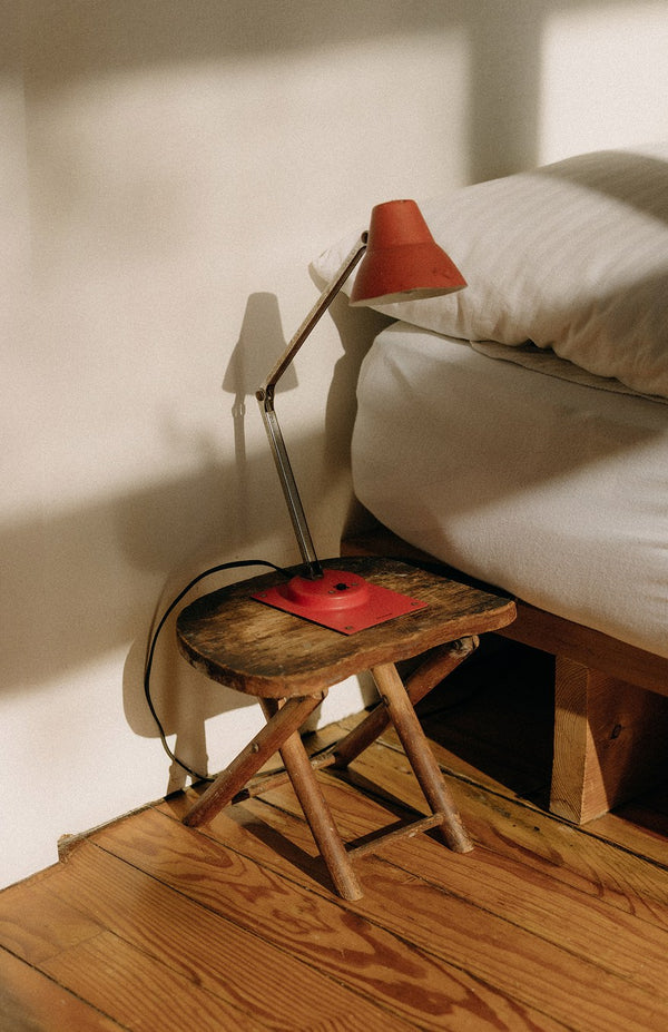 A wooden bedside table with a red lamp