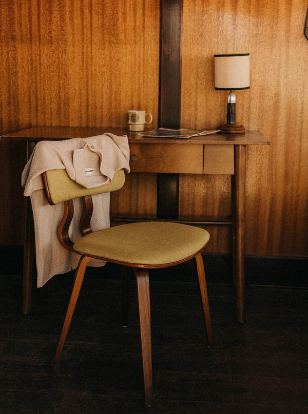 The Button Down Polo in Heather Oat draped over a mid-century modern chair