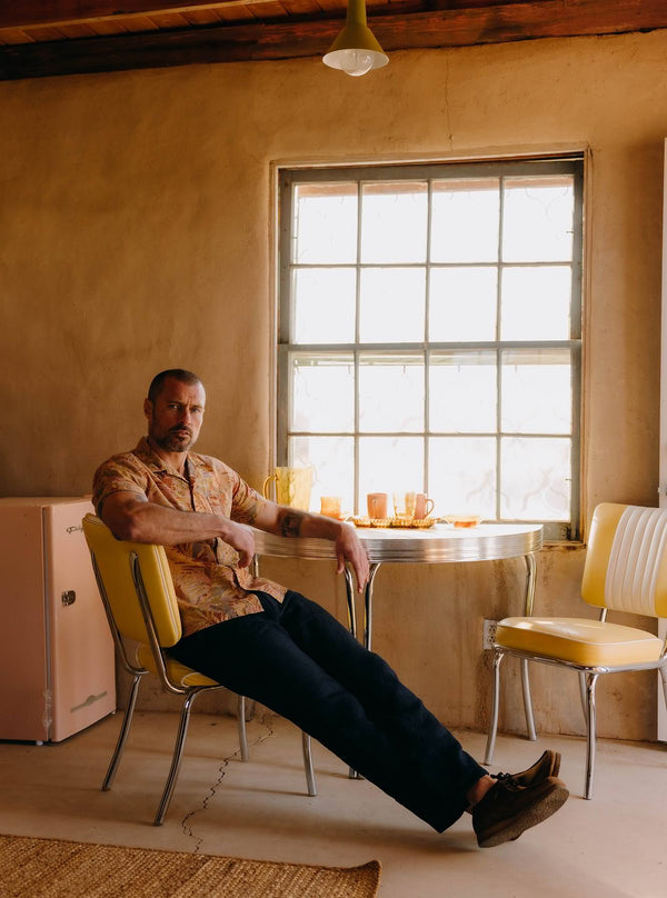 Model sitting at a vintage dining set, wearing The Hawthorne Shirt in Desert Palm
