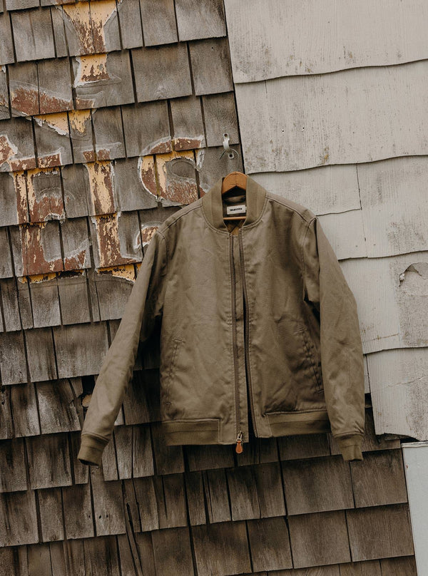 The Insulated Bomber Jacket in Fatigue Olive Dry Wax hanging on the wall